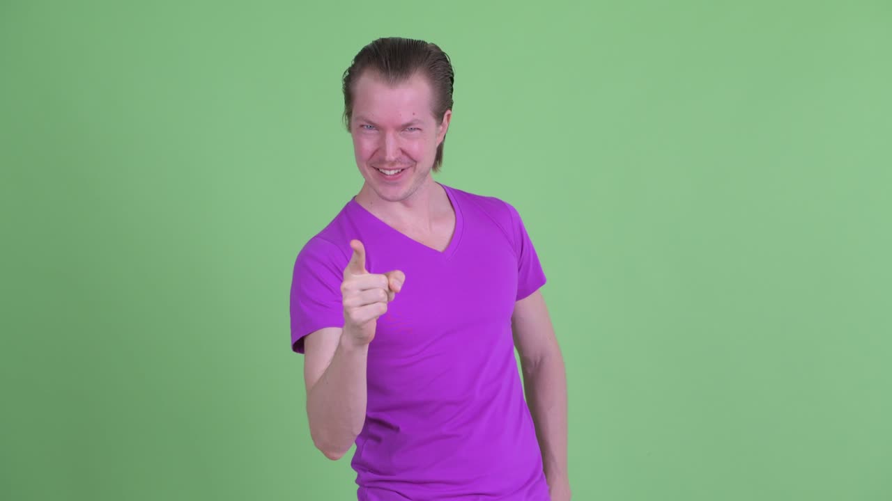 fotografía de estudio de un joven sonriendo y señalando con el dedo a la cámara contra un fondo verde