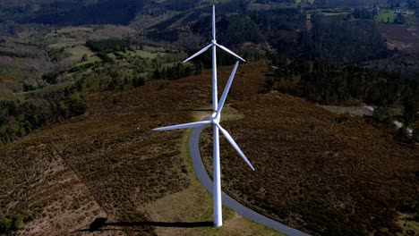 Two-wind-turbines-lined-up-spinning-their-blades-in-the-mountains-with-small-green-forests-of-trees-on-a-sunny-afternoon-of-blue-sky