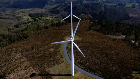 two wind turbines lined up spinning their blades in the mountains with small green forests of trees on a sunny afternoon of blue sky