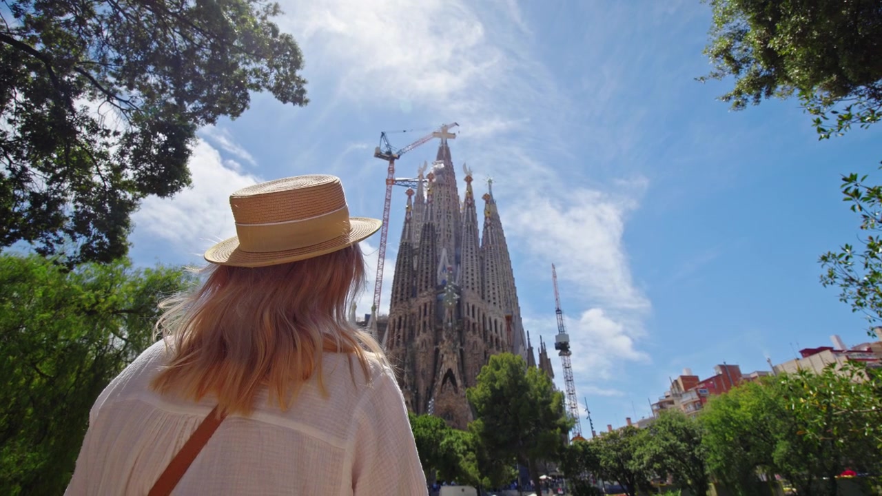 Nuori naisturisti ihailemassa Sagrada Familia -basilikaa Barcelonassa, Espanjassa aurinkoisena päivänä, ikoninen Gaudin maamerkki ja suosittu matkakohde Kataloniassa