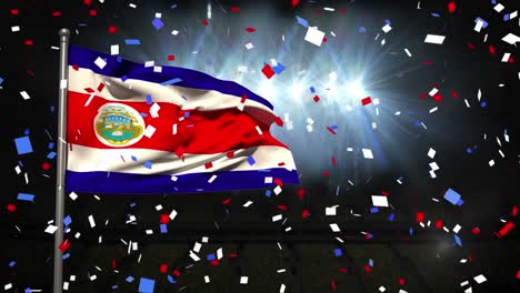 Animation-of-falling-confetti-over-waving-flag-of-costa-rica-on-pole-against-lights-in-stadium