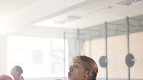 Mujer-Birracial-Inalterada-Enfocada-Levantando-Balón-Medicinal-En-Clase-De-Fitness-Grupal-En-El-Gimnasio,-En-Cámara-Lenta