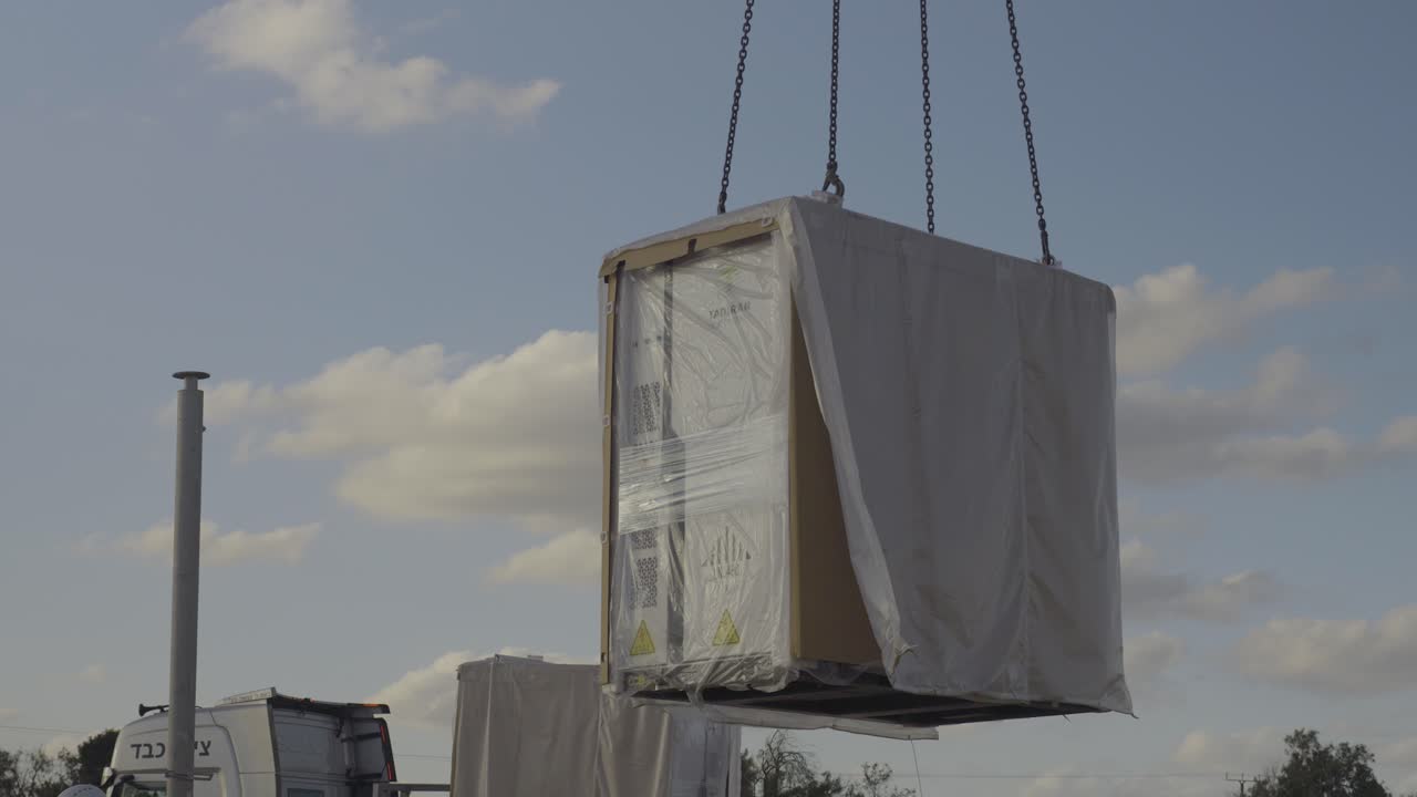 A protected electric cabinet is lifted by crane on a construction site, plastic moving with the wind - Israel