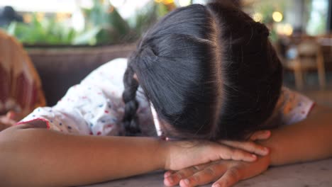 Young girl resting her head on her arms at a table