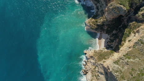 Vista-Aérea-De-Arriba-Hacia-Abajo-De-Una-Hermosa-Playa-Con-Aguas-Turquesas-Entre-Los-Acantilados-En-La-Costa-Mediterránea-De-España