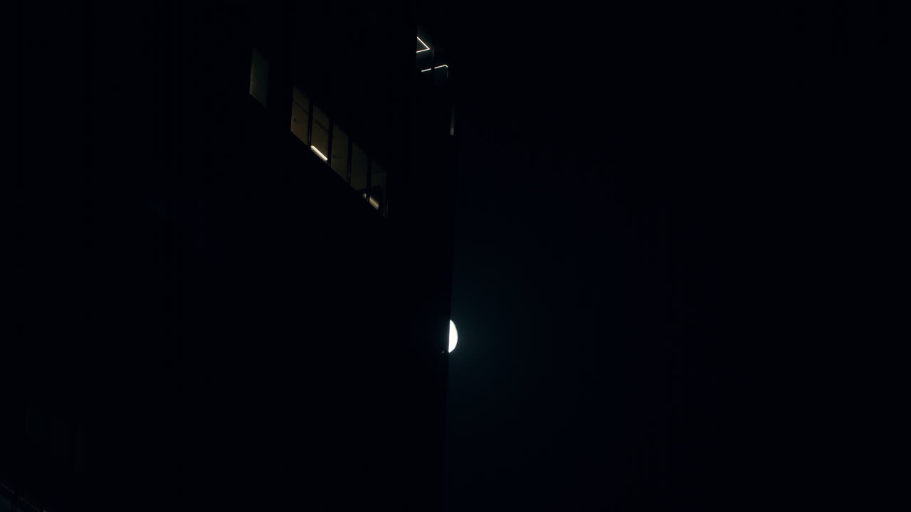 яркая луна на ночном небе медленно скрывается за зданием