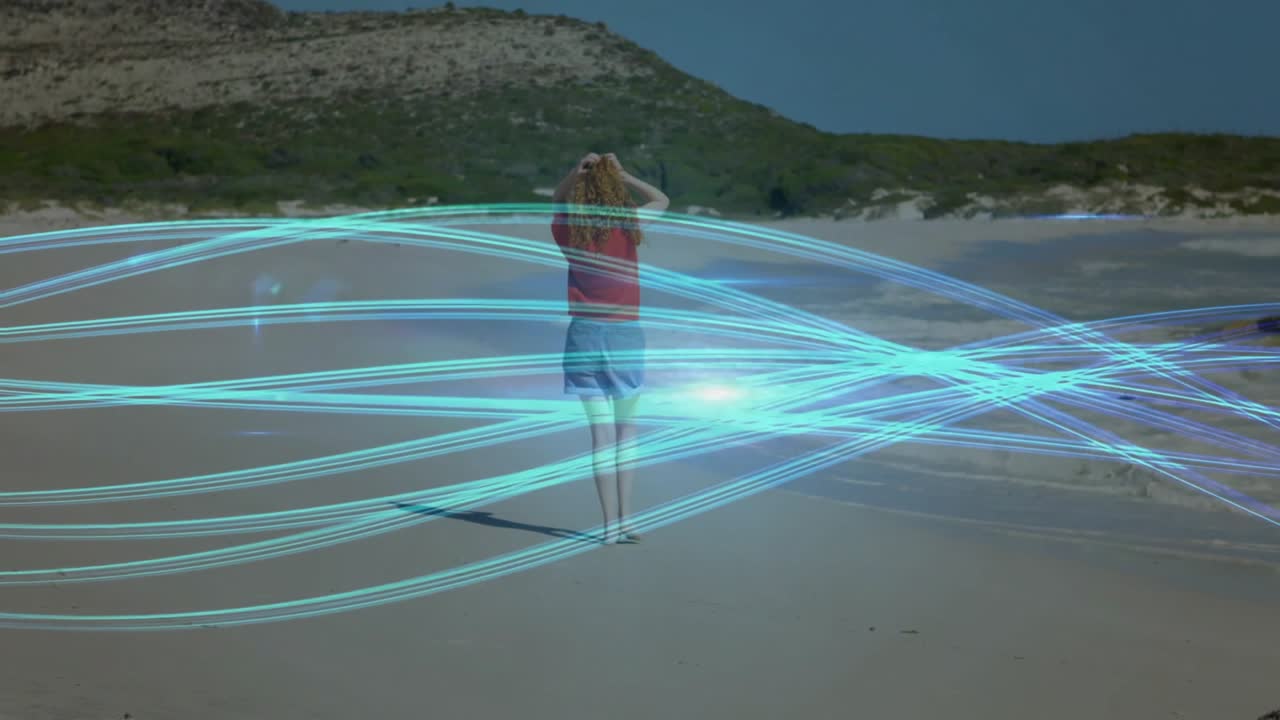 Woman walking on sandy beach raising hands behind head and causing swirling technology light orb
