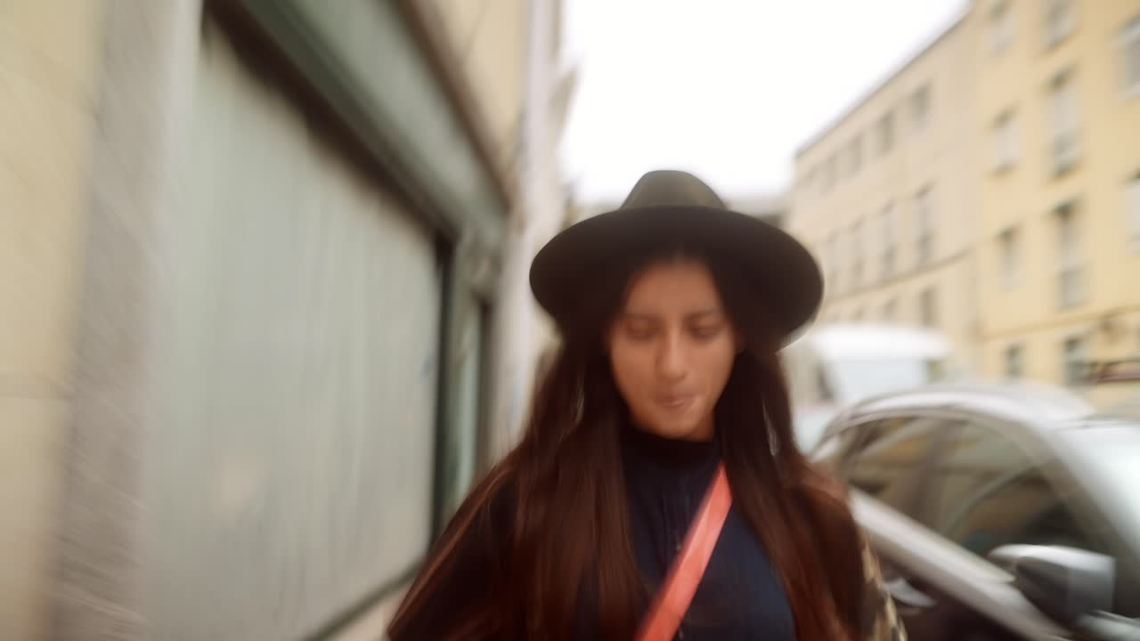 Giovane donna con cappello che passeggia felice per una strada di città