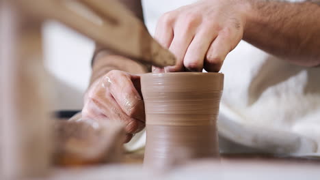 close up of hands of man wearing apron working at pottery wheel making vase in ceramics studio