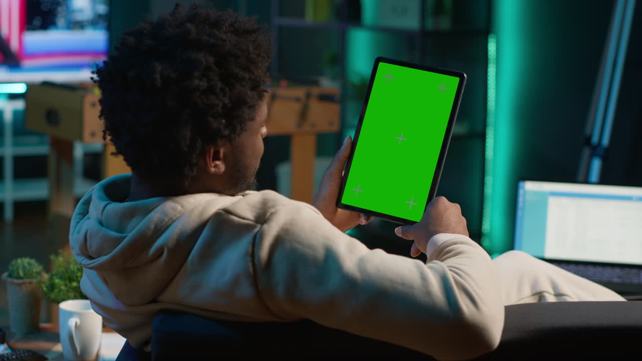 usuario de tecnología confiado mirando la pantalla de maqueta aislada en su sala de estar, relajándose con su trabajo remoto en el sofá. afroamericano adulto feliz navega por internet. cámara a.