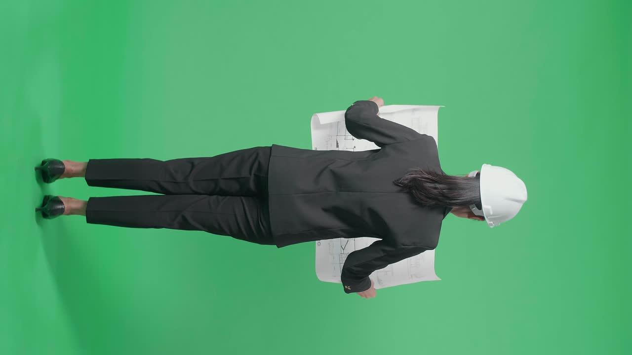 Full Body Back View Of Asian Female Engineer Looking At Blueprint Before Looking Around And Shaking Her Head In The Green Screen Studio