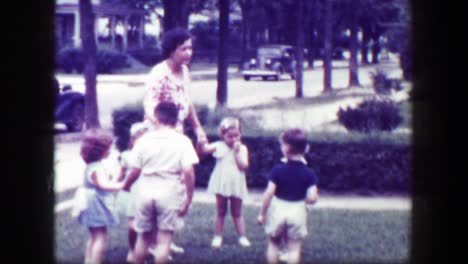 1949: schoolmarm teacher playing kids front yard holding hands.