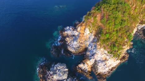 Aerial-drone-shot-looking-down-in-a-steep-rocky-cliff-at-the-point-of-a-calm-water-bay-in-Carrizal-off-the-coast-of-Mexico