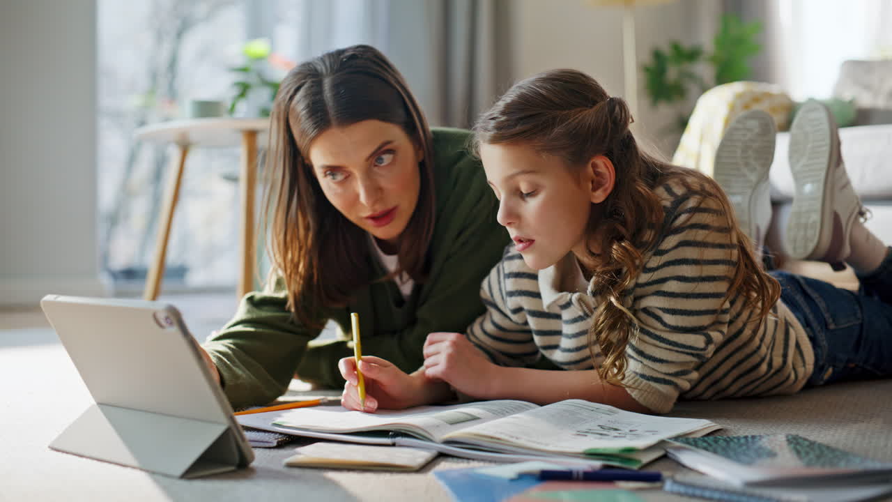 Tata e bambino studiano una lezione scolastica online sdraiati sul pavimento dell'appartamento, primo piano.
