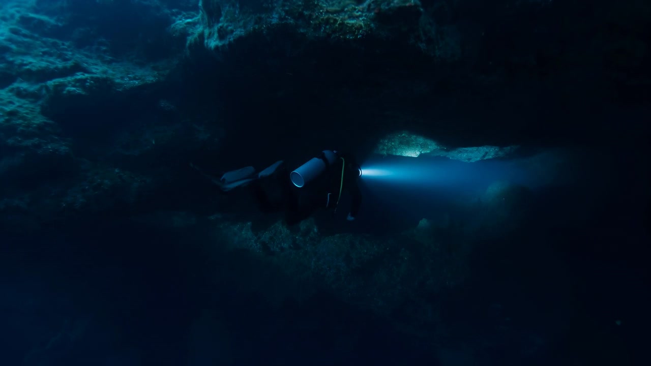 Scuba Diver Exploring Underwater Cave Blue Torch Beam Illuminates Rocky Grotto And Silent Seabed Technical