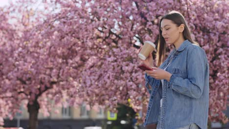 young woman enjoying coffee and phone in a spring park