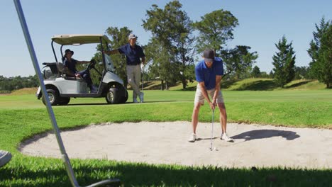 hombre mayor caucásico golpeando una pelota de golf fuera de una trampa de arena en un campo de golf en un día soleado y brillante