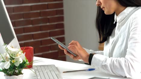 mujer de negocios usando un teléfono móvil mientras trabaja en la computadora