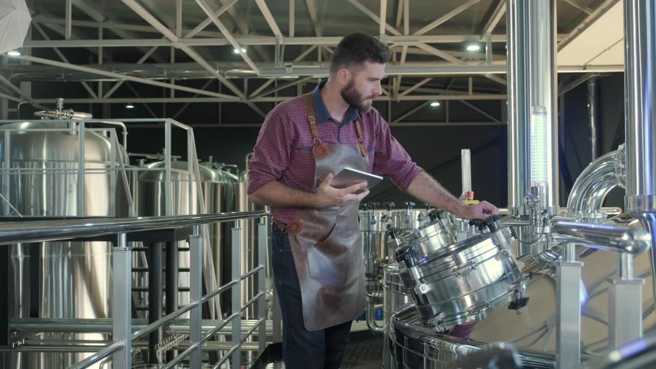 un joven cervecero con un delantal de cuero supervisa el proceso de fermentación de la cerveza en una fábrica de cerveza moderna