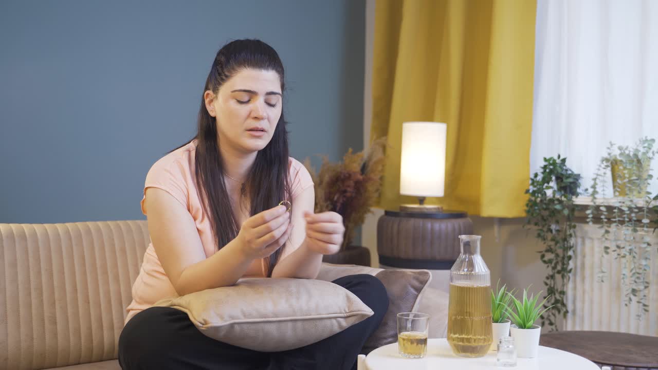 mujer pensativa con anillo de bodas en la mano bebiendo alcohol.