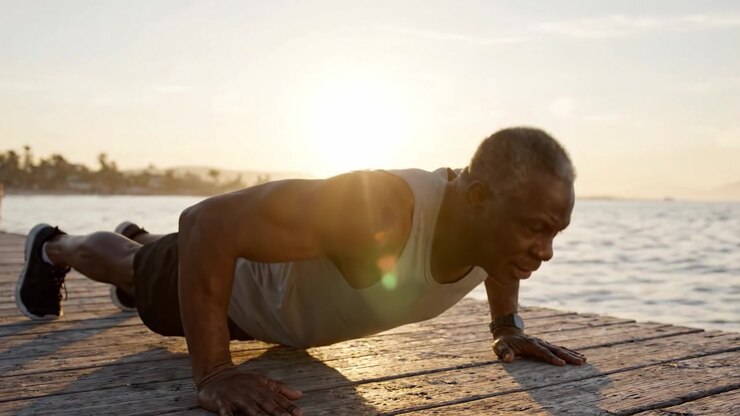 A determined individual performs push-ups on a wooden dock at sunset, showcasing strength and dedication against a serene water backdrop during golden hour.