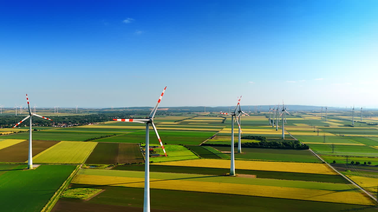 Wind turbines produce clean power. Green fields stretch across the landscape dotted with wind turbines harnessing renewable energy under a clear blue sky