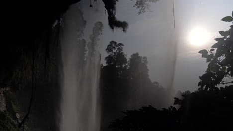 the silhouette of a water fall as the sun shines through in a jungle valley in east africa