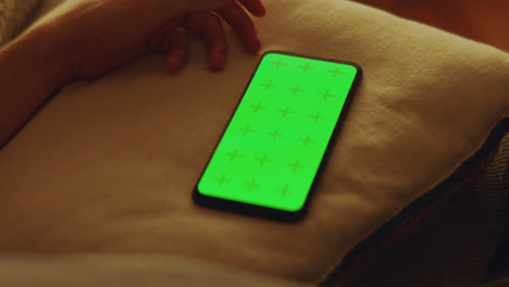 persona sosteniendo un teléfono inteligente con una pantalla verde en una almohada