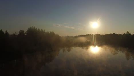 Misty-morning-sunlight-over-autumn-forest-lake-and-scenic-countryside-landscape-aerial-wide-view