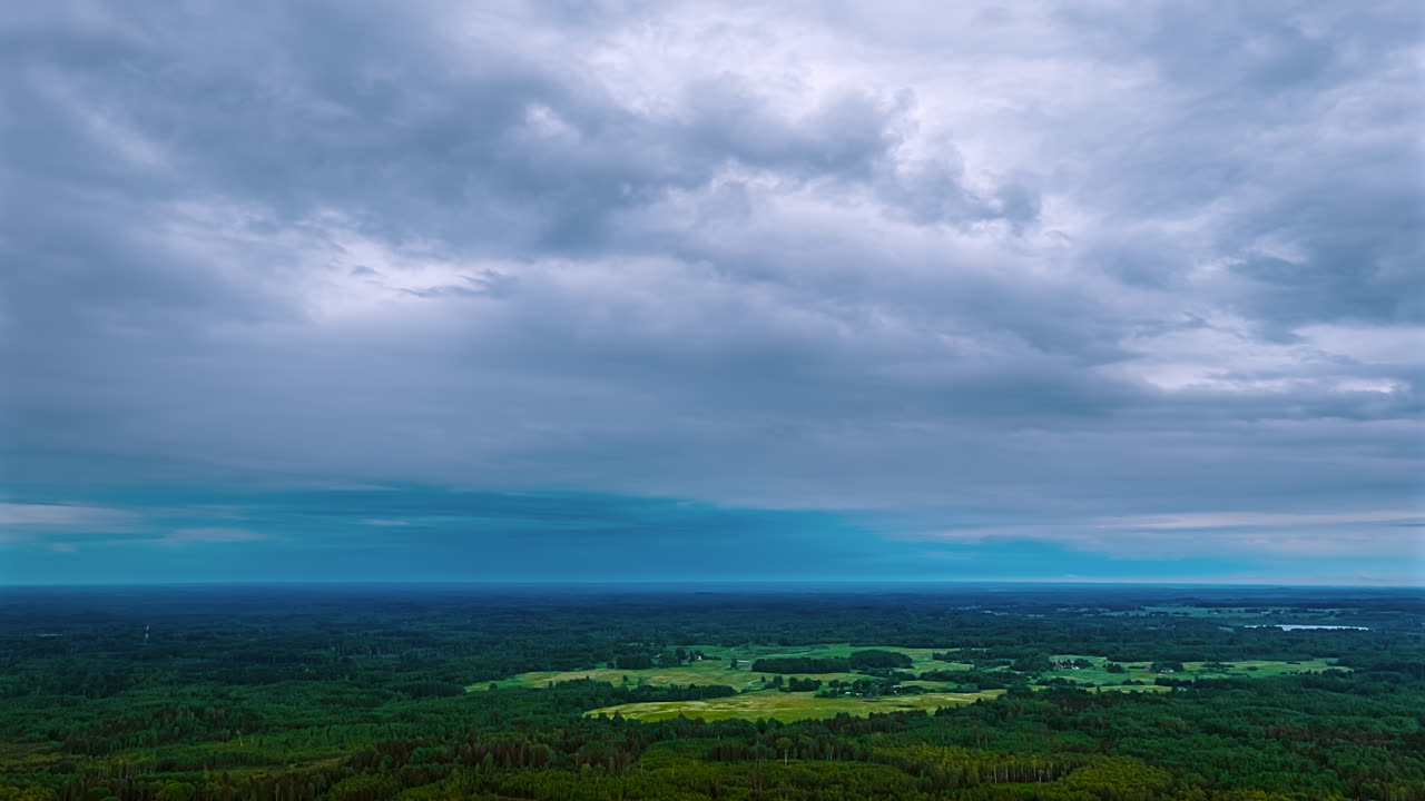 An atmospheric aerial timelapse captures moody grey clouds moving across the sky at dusk above a vast and endless wilderness landscape of dark green forests