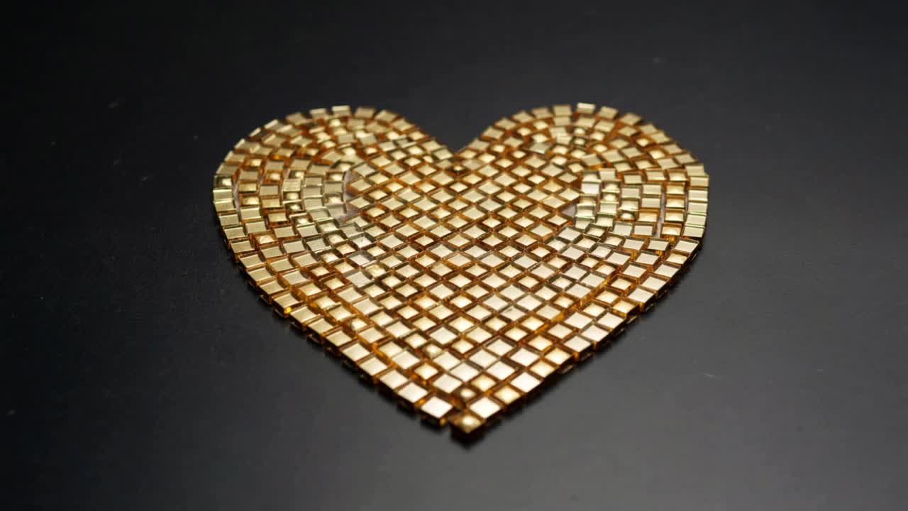 Carrello della camera che zooma su mosaico a cuore dorato su superficie riflettente nera, enfatizzando le tessere luccicanti