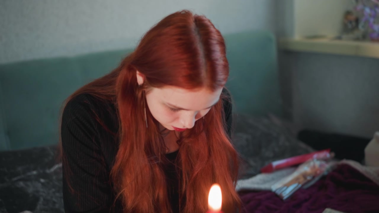 Donna bianca dai capelli rossi che fissa una candela, pratica di divinazione privata in camera da letto da parte di una studentessa, profilo di un'amica che osserva, fiamma tremolante che si riflette su un quaderno, luce ambientale calda, intima e contemplativa.