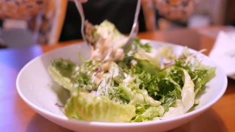 mezclar un tazón lleno de ensalada de verduras mezcladas y aderezar usando cuchara y tenedor