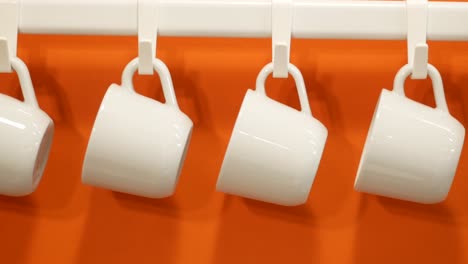 white mugs hanging on a rack against an orange wall