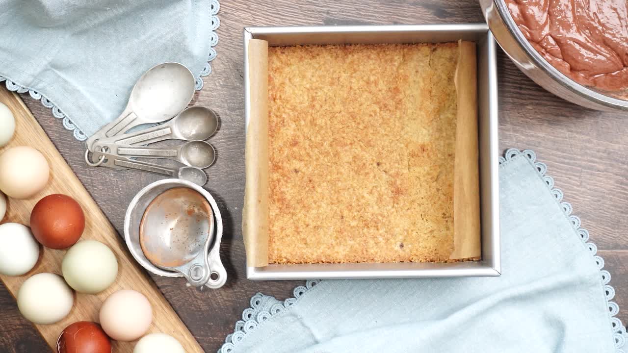 Pressing in the pastry crust into a square baking pan to make pecan caramel brownies. Making a dessert with a pastry crust on the bottom. Pie or cookie crust being pressed into a baking pan.
