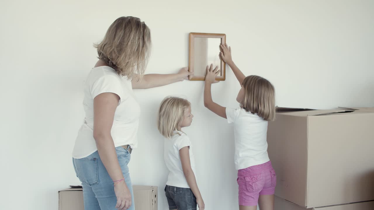 dos niñas y su madre eligiendo un lugar en la pared para la imagen