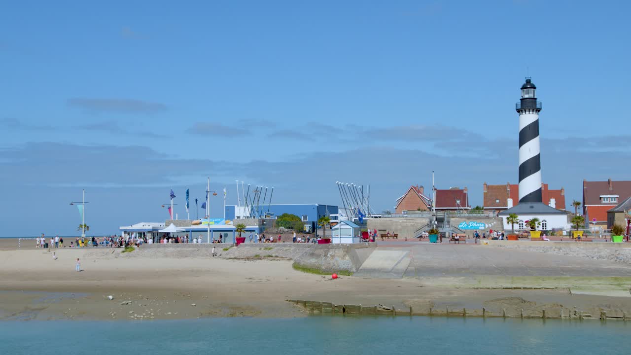 Lighthouse, beach, and town viewed in daylight with static camera and clear blue sky