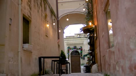 Mesas-Y-Luces-En-Un-Callejón-En-Matera,-Italia-Con-Filmación-De-Establecimiento