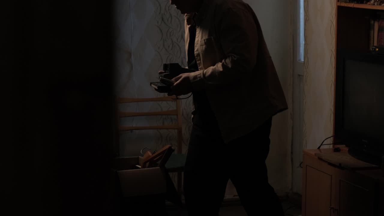 um homem recolhe coisas velhas numa caixa para se mudar de sua antiga casa. ele deixa seu antigo apartamento e está triste