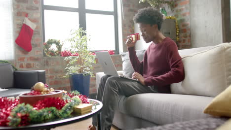 happy african american man sitting on sofa using laptop for video call at home, slow motion