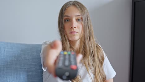 mujer cambiando de canal de tv usando el control remoto de tv, mirando a la cámara, primer plano