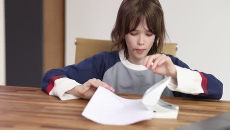 young person using a paper hole puncher at a wooden table