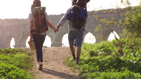 young lovely couple backpackers tourists walking holding hands toward roman aqueduct arches in parco degli acquedotti park ruins in rome on romantic misty sunrise with guitar and sleeping bag slow motion