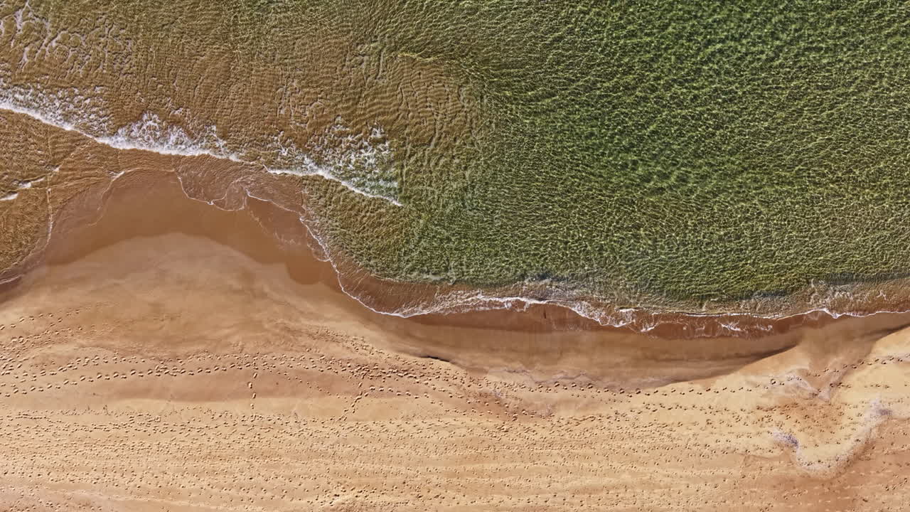 Waves gently lap against the golden shore as footprints mark the sandy beach on a sunny afternoon near the coastline