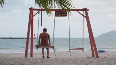 Mann-Sitzt-Auf-Einer-Schaukel-Und-Genießt-Die-Aussicht-Auf-Den-An-Hai-Strand-Vom-Sandstrand-In-Con-Dao,-Vietnam