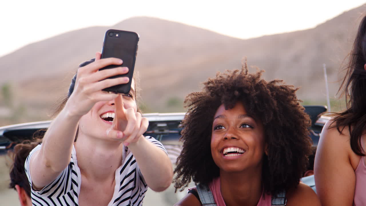 Amiche che si scattano un selfie sul sedile posteriore di un'auto decappottabile.