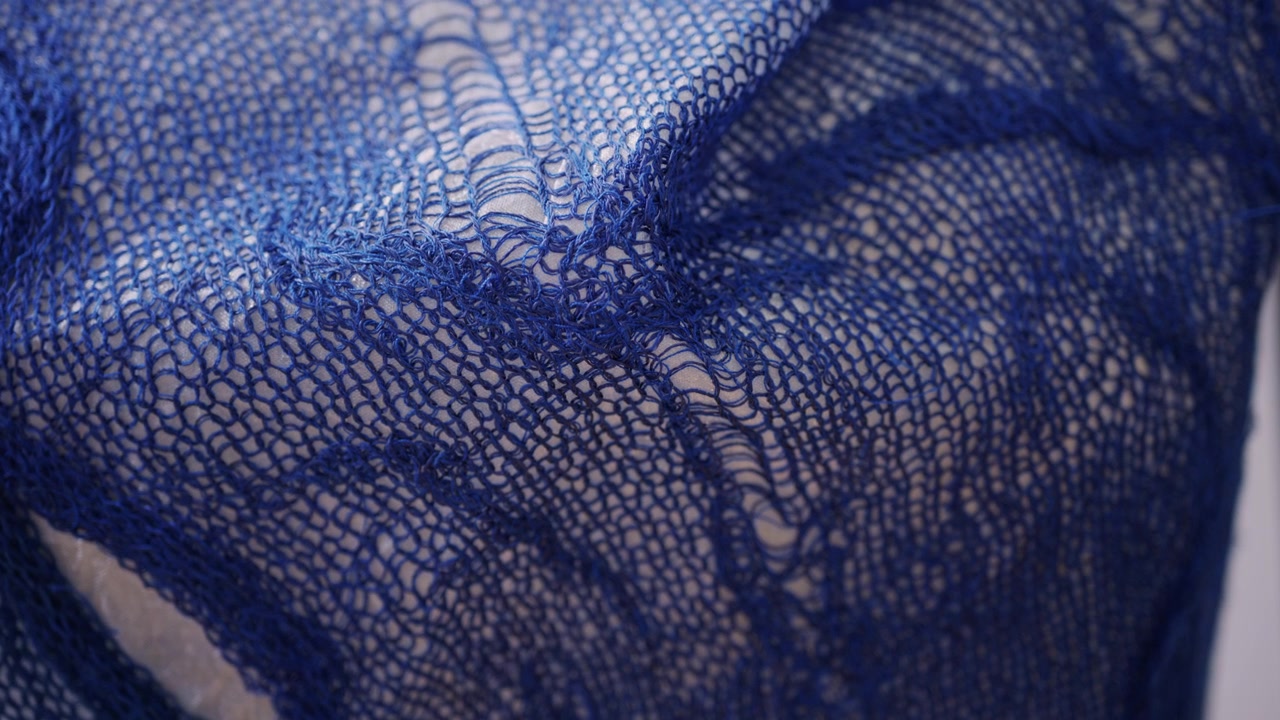 Close up of a blue openwork knitted textile stretched over a white form