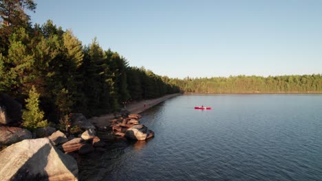 high aerial of red canoe on pristine wilderness lake at golden hour