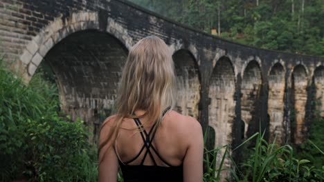 a captivating scene in ella, sri lanka, where a woman in the lush jungle, gazing towards the iconic nine arches bridge.
