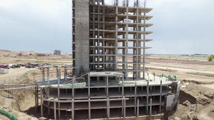 Tall concrete tower frame rises from a large foundation at an active construction site
